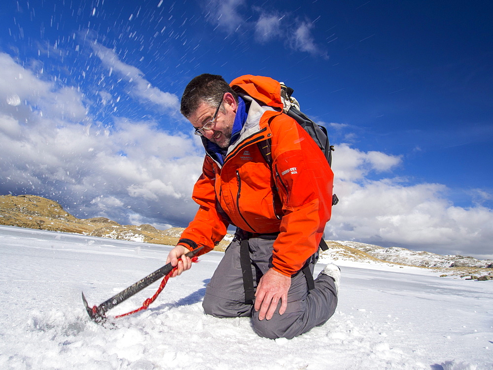 A mountaineer testing the thickness of ice on Sprinkling Tarn to see if it is safe to walk on, Lake District, Cumbria, England, United Kingdom, Europe