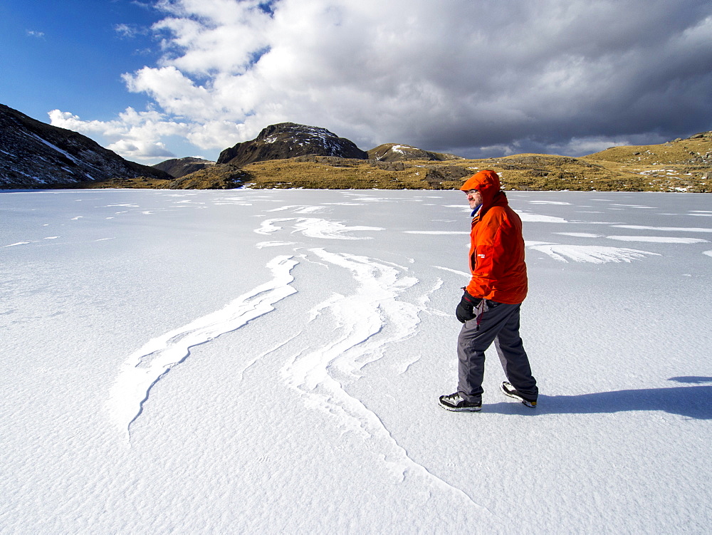 A climber on Sprinkling Tarn at the head of Borrowdale, looking towards Great End, with drifted snow making patterns on the ice, Lake District, Cumbria, England, United Kingdom, Europe