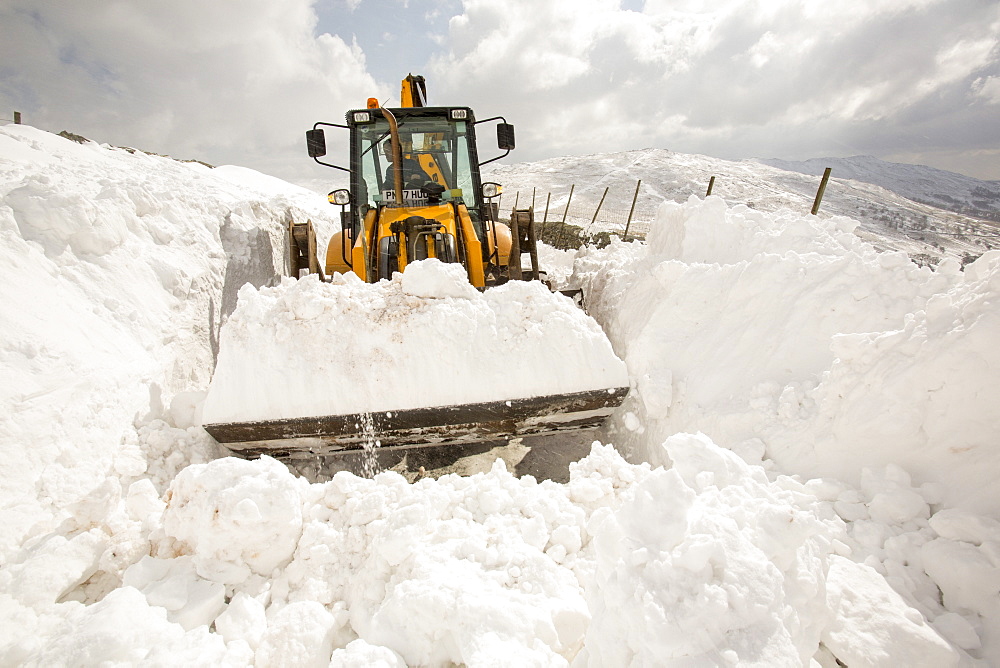 A JCB tries to clear a way through massive snow drifts blocking the Kirkstone Pass road above Ambleside in the Lake District, Cumbria, England, United Kingdom, Europe