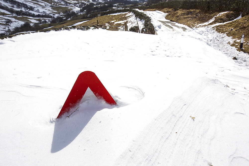 The tip of a road sign pokes out of massive snow drifts blocking the Kirkstone Pass road above Ambleside in the Lake District, Cumbria, England, United Kingdom, Europe