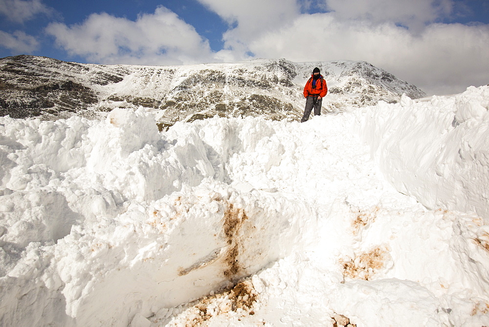 A walker on top of massive snow drifts blocking the Kirkstone Pass road above Ambleside, Lake District, Cumbria, England, United Kingdom, Europe