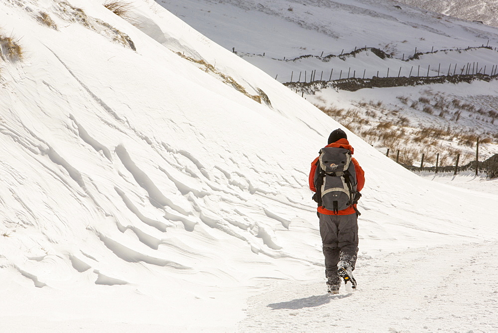 A walker passes massive snow drifts blocking the Kirkstone Pass road above Ambleside in the Lake District, Cumbria, England, United Kingdom, Europe