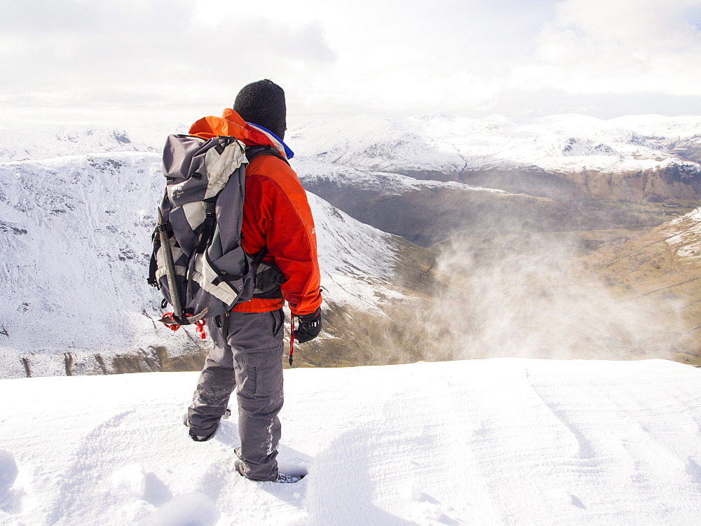 A walker on Gray Crag being battered by spindrift looking towards the Helvellyn rang during unseasonally cold weather in late March 2013, Lake District, Cumbria, England, United Kingdom, Europe