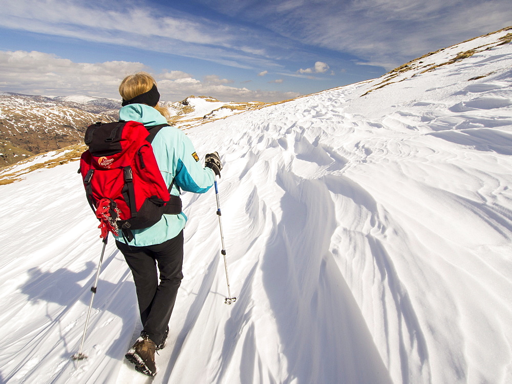 Snow shaped and scoured by a strong wind when it fell, and fell walker above Wrynose Pass in the Lake District, Cumbria, England, United Kingdom, Europe