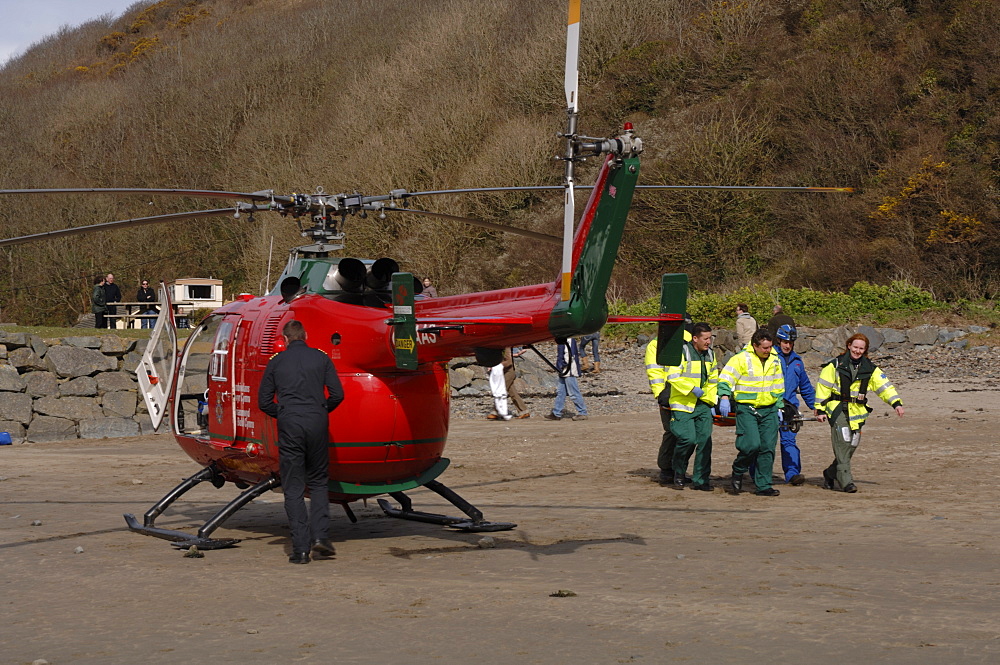 South Wales Air Ambulance helicopter and crew carrying a casualty on a stretcher at Solva harbour, Solva, Pembrokeshire, Wales, UK, Europe