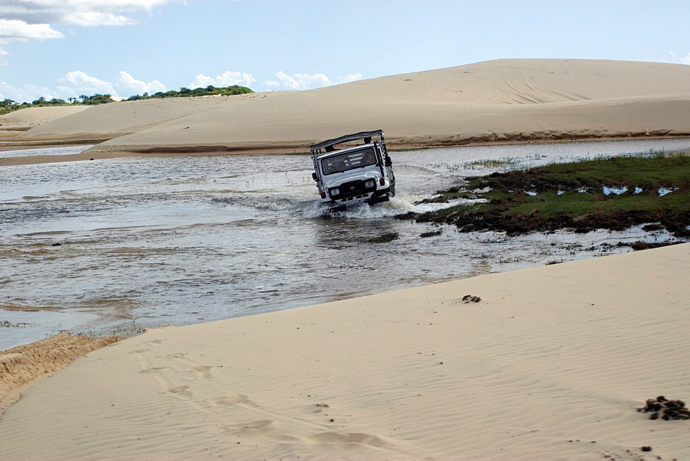 Off-road truck trespassing one of the many lakes formed by rainfall on Lencois Maranhenses, Tutoia, Maranhao, Brazil, South America