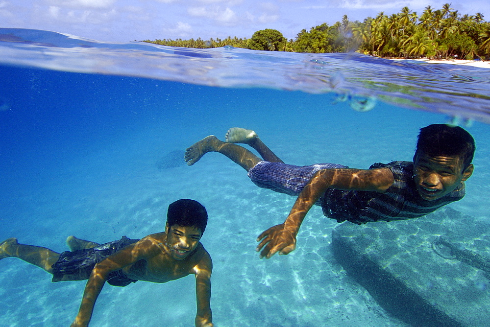 Marshallese boys smiling underwater and coconut trees lining the shore of Majikin Island, Namu atoll, Marshall Islands, Pacific