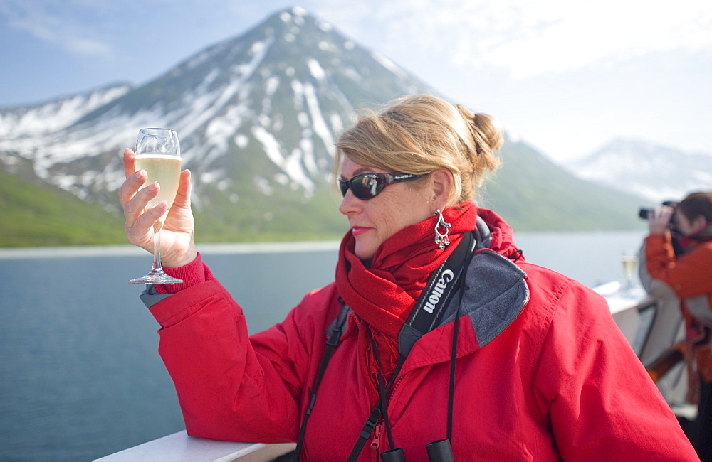 Views from the Clipper Odyssey towards Russkaya Bay of volcanic mountains in mist and sun set, Woman with champagne, Russkaya Bay (Bering Sea), Russia, Asia.