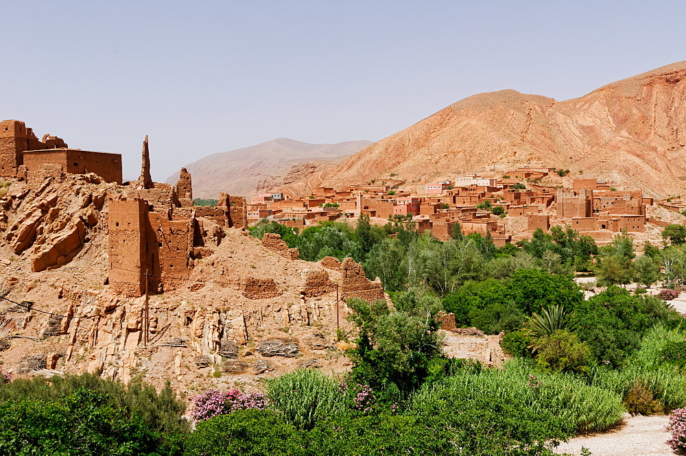 Green vegetation on the stream banks contrasts with the bare rock and mud bricks of ancient ruins and a mountain village, near the Dades Gorge, Morocco, North Africa, Africa