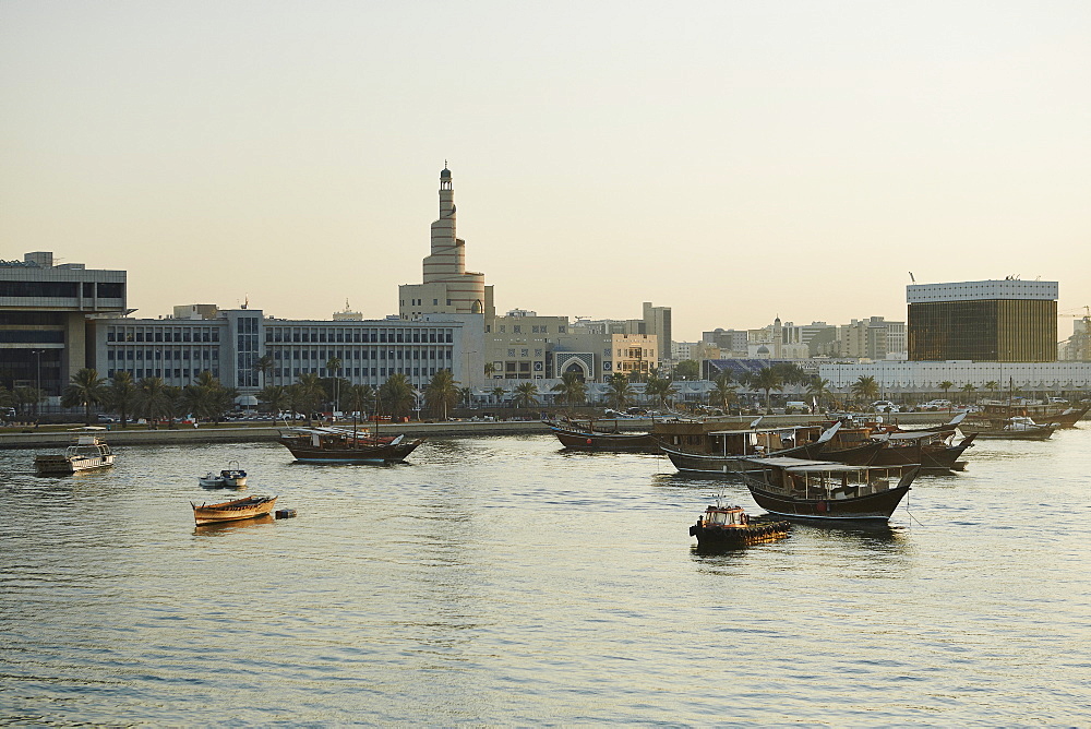 View from The Museum of Islamic Arts towards old Doha and The Islamic Centre with dhows moored in the Harbour at sunset, Doha, Qatar, Middle East