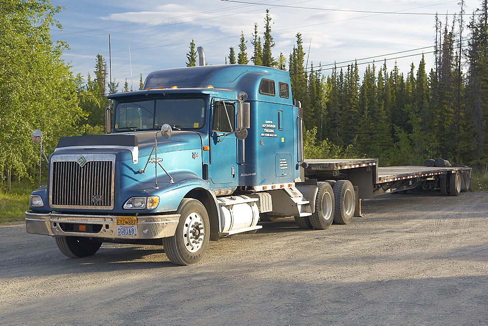 Blue Eagle, American Tractor with trailer attached.  Parked up in a layby next to a forest.  Sunny in the Alaskan Interior. The Interior, Alaska, USA