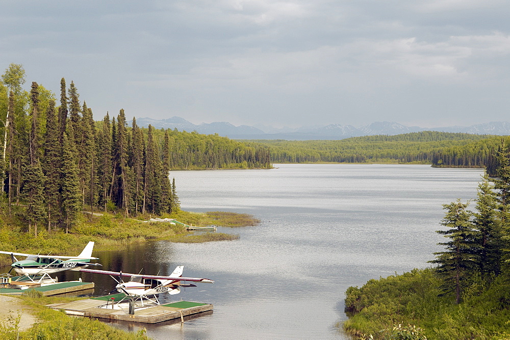 Two Boat Planes moored on an Alsakan Lake, surrounded by a  forrest.  The sky is heavy with cloud, good chance of rain.  Located in the Interior region of Alaska. The Interior, Alaska, USA