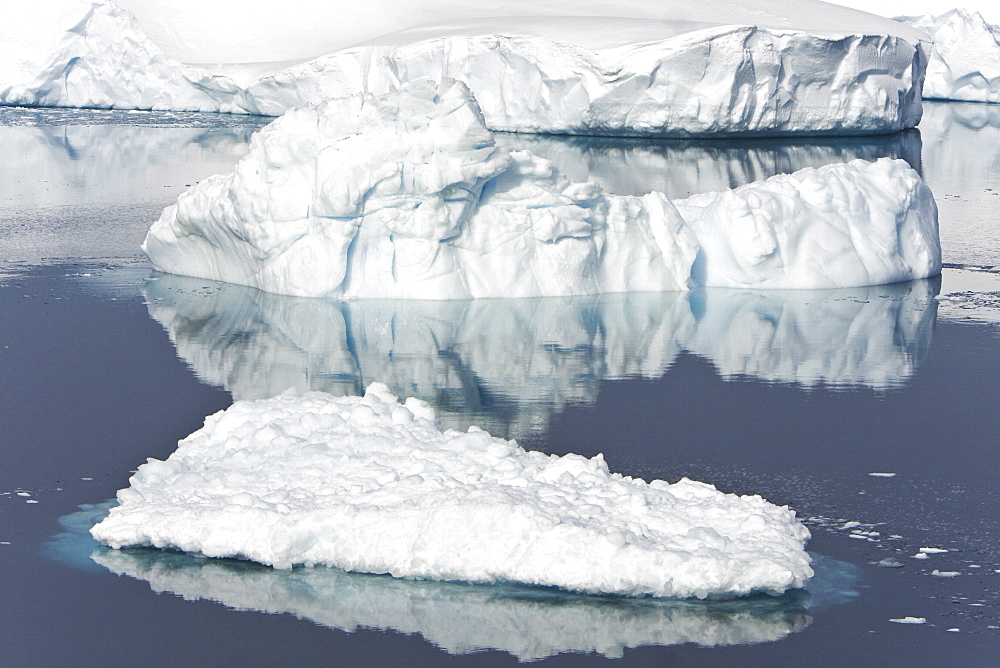 Icebergs and brash ice reflected in calm waters on the west side of the Antarctic peninsula, Antarctica.