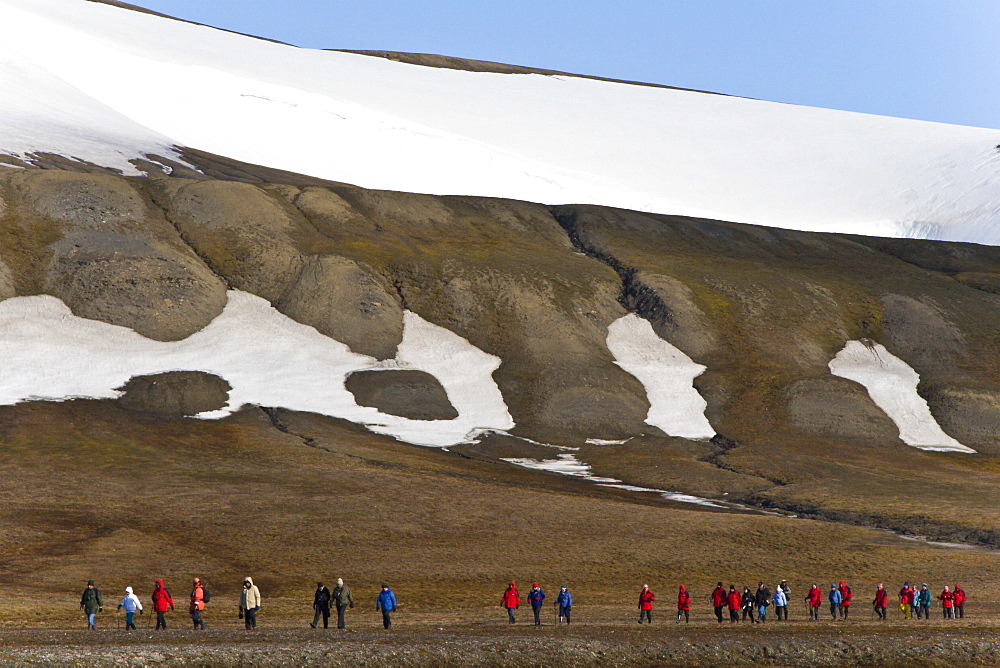 Hikers walking over open tundra beneath ice covered hills surrounding the Rosenberg Valley on EdgeØya Island in the Svalbard Archipelago in the Barents Sea, Norway.