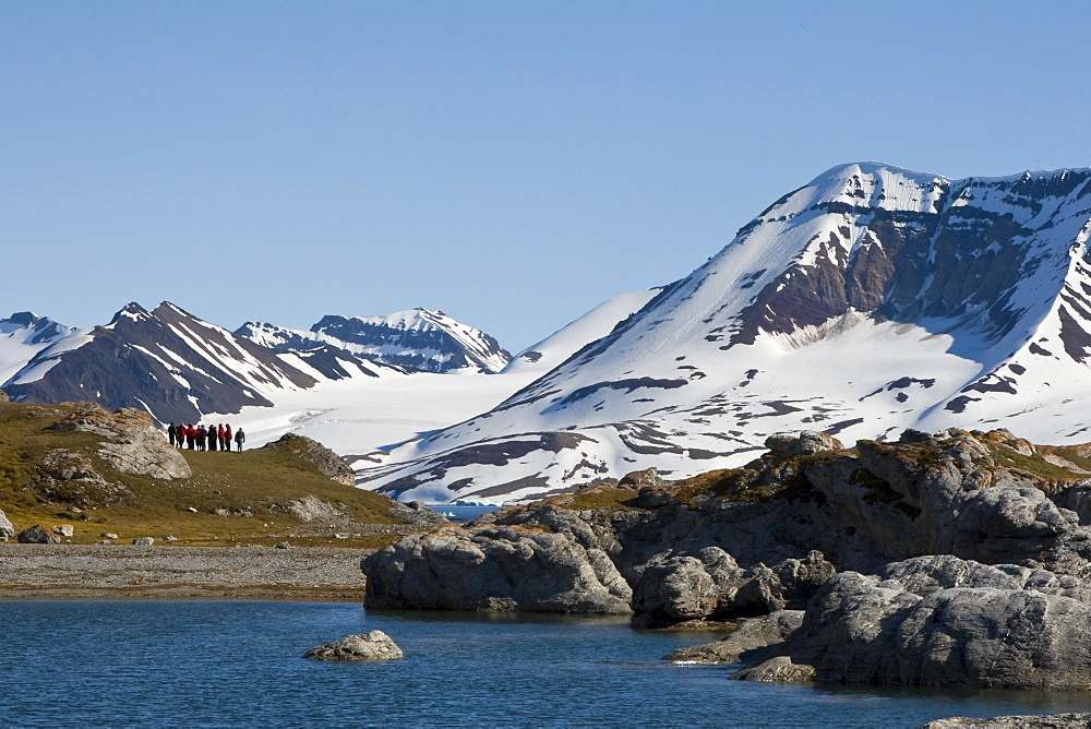 A view of hikers in front of the towering cliff and glacier in Hornsund (Horn Sound) on the southwestern side of Spitsbergen Island in the Svalbard Archipelago, Barents Sea, Norway.