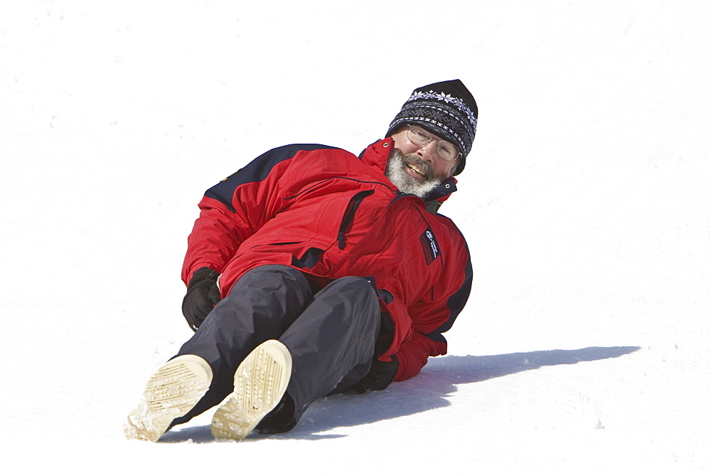 Lindblad Expeditions guests sliding down a hill on their snow pants in Antarctica as part of expedition travel. NO MODEL RELEASES FOR THIS IMAGE.