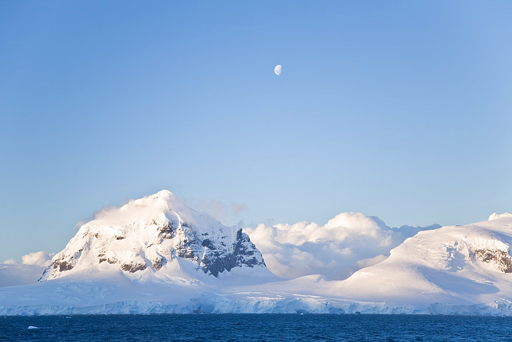 The Lindblad Expedition ship National Geographic Explorer in Dahlman Bay in late evening light as the waxing moon rises on the west side of the Antarctic Peninsula in Antarctica. 