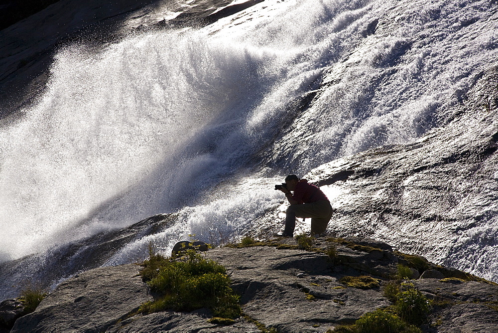 A photographer at a snow melt waterfall in Nordfjord, an arm of the larger Melfjord - situated just above the Arctic Circle - in northern Norway, Barents Sea.