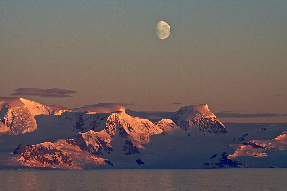 The Lindblad Expedition ship National Geographic Explorer in Dahlman Bay in late evening light as the waxing moon rises on the west side of the Antarctic Peninsula in Antarctica. 