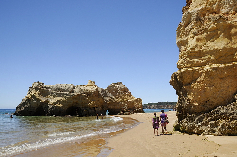 People walking and paddling near sandstone cliffs and rocks at Praia da Rocha beach, Portimao, Algarve, Portugal, Europe