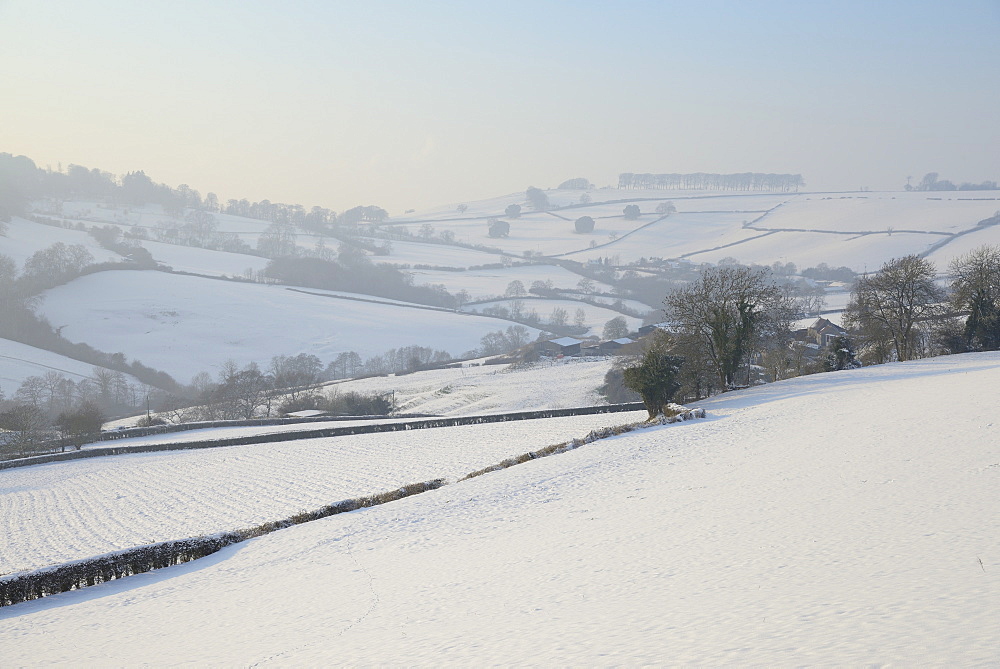 Snow covered hillside pastureland, arable fields and bare trees in winter, Tadwick, Bath and Northeast Somerset, England, United Kingdom, Europe