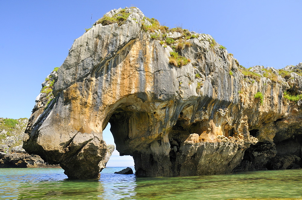 Natural rock archway carved by the sea through karst limestone rock at Cuevas del mar (sea caves) beach, near Llanes, Asturias, Spain. 