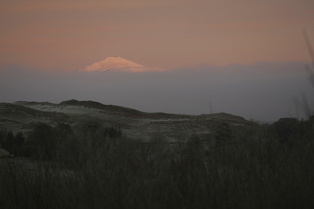 Ben Cruachan with sun breaking through cloud illuminating mountain top, creating pink glow. Taken from Kilchrenan view point. Argyll, Scotland