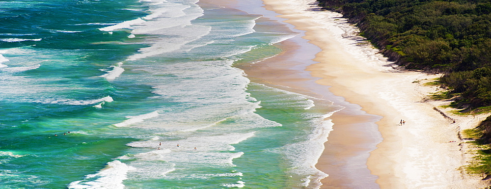 Panoramic photo of surfers heading out to surf on Tallow Beach at Cape Byron Bay, New South Wales, Australia, Pacific