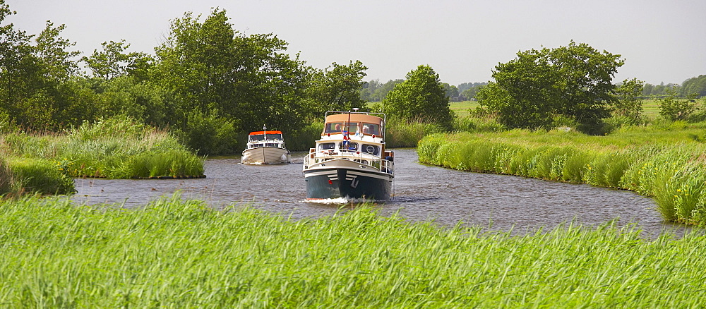 Two houseboats driving on the river Grecht under grey sky, Netherlands, Europe