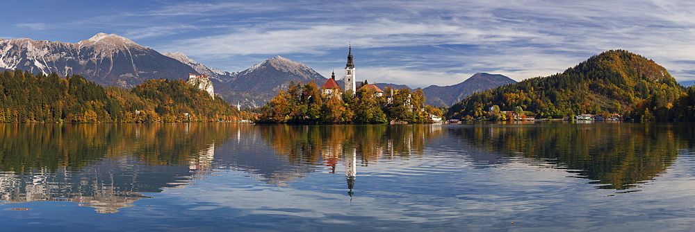 Picturesque view of St. Mary's Church and its reflection in the Lake Bled in autumn, in the background the castle of Bled soars in front of the Julian Alps, Gorenjska, Slovenia