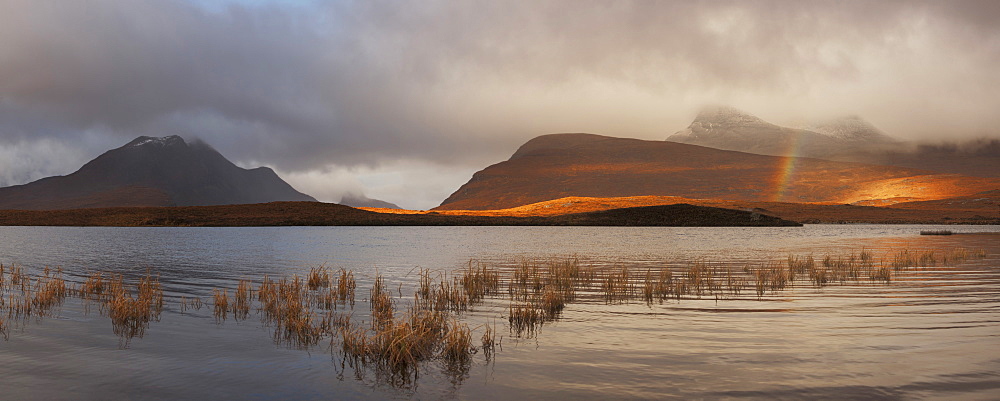 View from Lochan an Ais to the peaks of the Inverpolly Nature Reserve with a rainbow over the lake, Ullapool, Sutherland, Scotland, United Kingdom