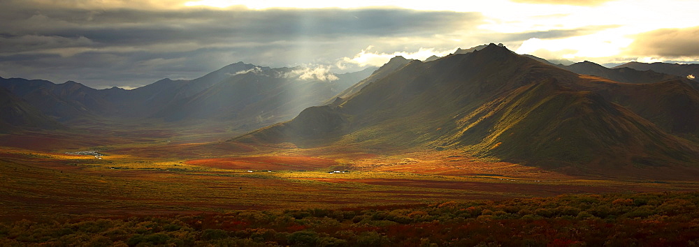 Panoramic image of the Cloudy Range with shafts of sunlight hitting the fall colours of the Dempster Highway, Yukon