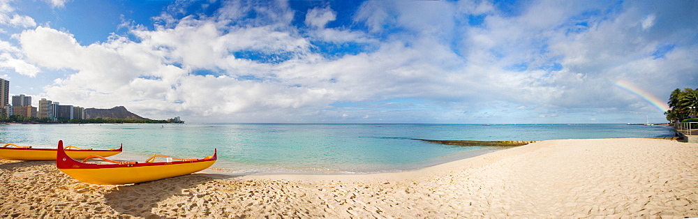 Hawaii, Oahu, Waikiki, Outrigger canoes on the beach with a rainbow and Diamond Head in the background.