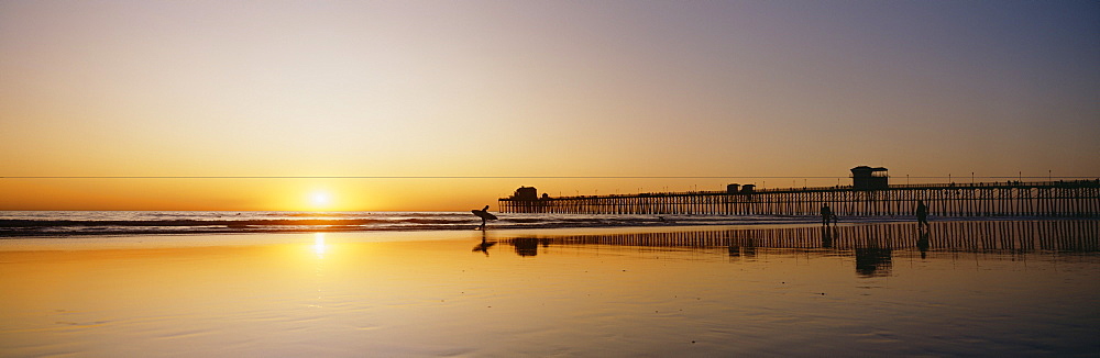 California, Oceanside Pier and surfers silhouetted against sunset, Reflections on beach.