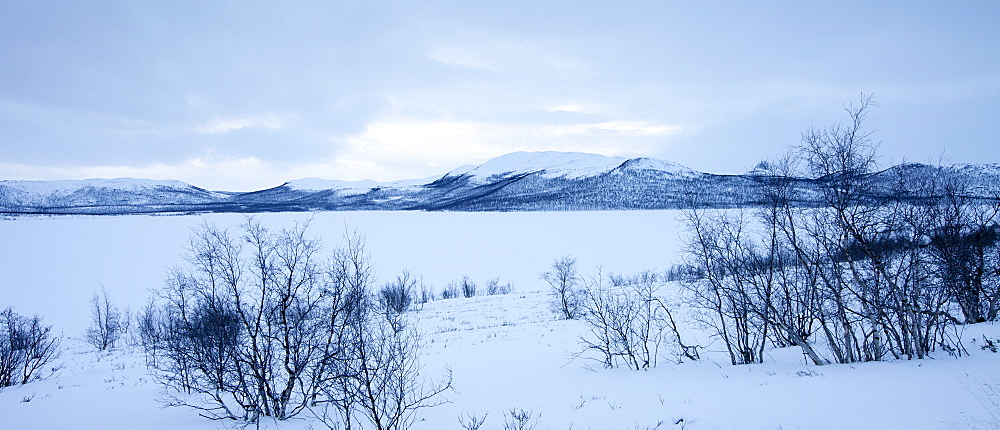 Frozen Kilpisjarvi lake with Sweden in the background in arctic wilderness at nightfall by Kilpisjarvi, Finland