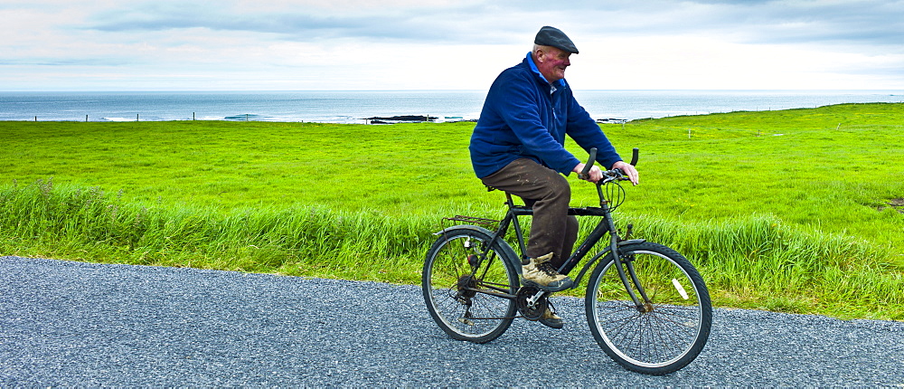 Local Irish man cycling traditional bicycle along country lane in County Clare, West of Ireland