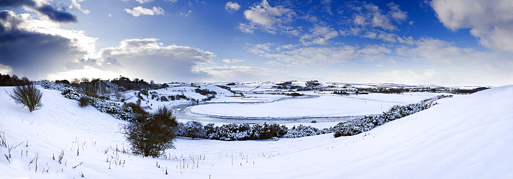 Panoramic view of snow-covered landscape beneath blue winter sky looking towards meandering River Aln, Lesbury, near Alnwick, Northumberland, England, United Kingdom, Europe