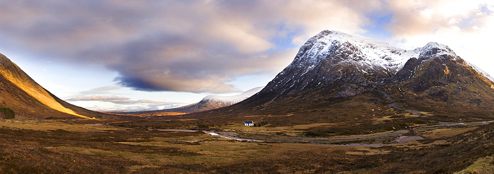 Winter panoramic view of Rannoch Moor showing lone whitewashed cottage on the bank of a river, dwarfed by snow-covered mountains, Rannoch Moor, near Fort William, Highland, Scotland, United Kingdom, Europe