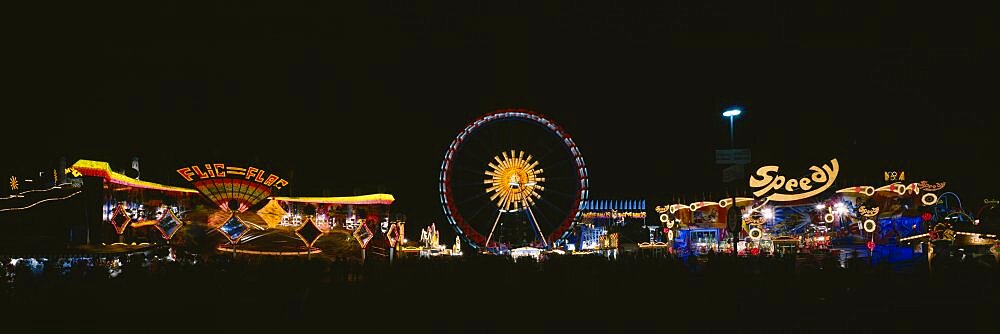 Ferris wheel and neon signs lit up at night in an amusement park, Oktoberfest, Munich, Germany