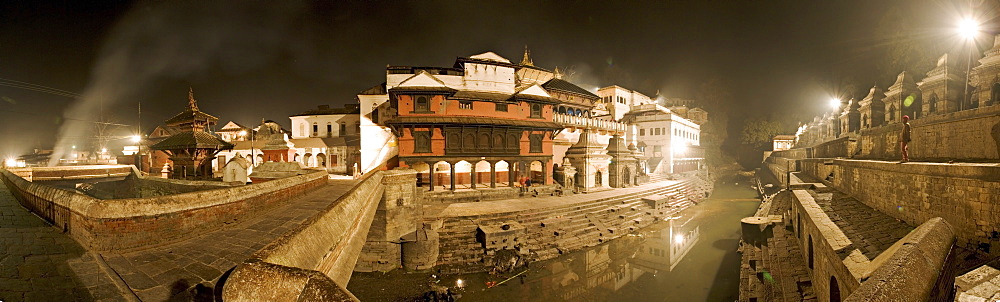 Smoke from funeral pyres on the ghats on the left drifts across the bridge over the river Bagmati at Nepal's holiest Hindu pilgrimage site, Pashupatinath, Kathmandu, Nepal, Asia