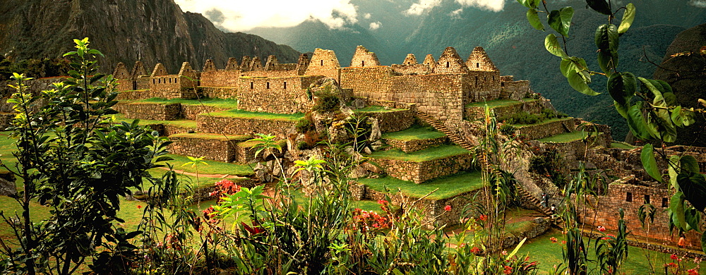 Machu Picchu the ancient city with Huayna Picchu Peak beyond view past tropical foliage toward structures in Common District, Highlands, Peru