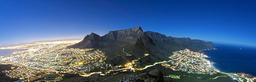 Panoramic view of Table Mountain and the city of Cape Town in moonlight. Table Bay can be seen far left and the Atlantic Ocean coastline and suburb of Camps Bay and its beach can be seen far right.