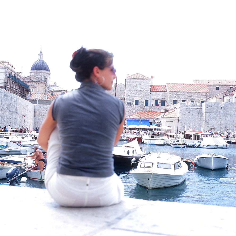 Female tourist sitting at harbour near city wall, Dubrovnik, Dalmatia, Croatia