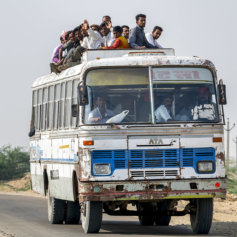 A bus full of people and passengers riding on the roof, Jaisalmer, Rajasthan, India