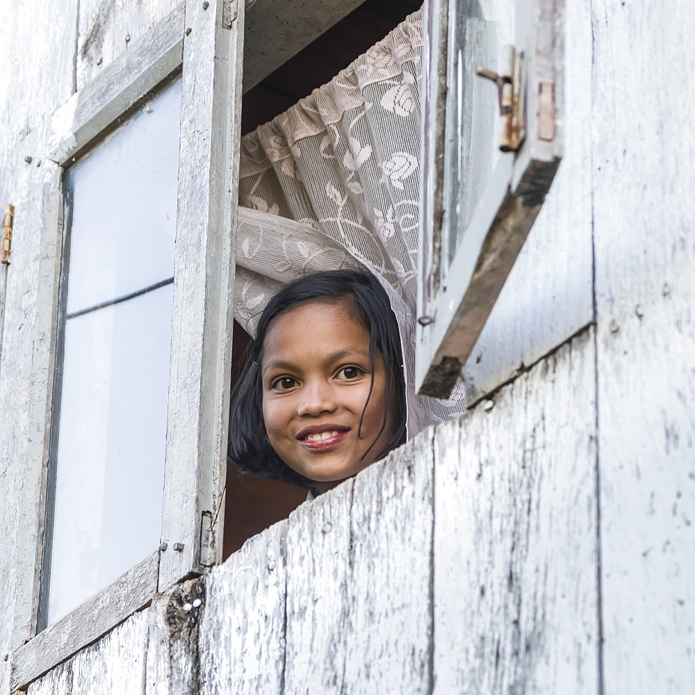 A girl looks out an open window and smiles as she looks down at the camera, Sikkim, India