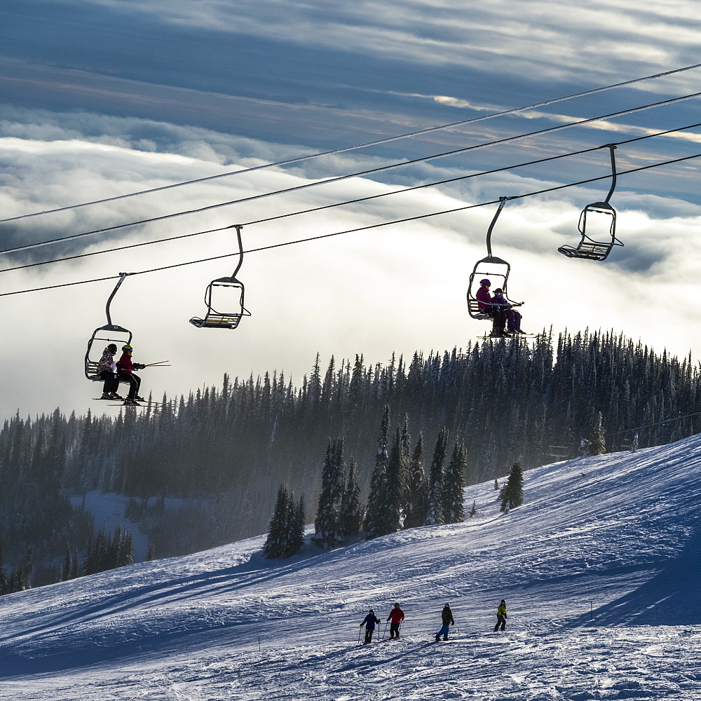 Skiers on a chairlift and on the slope below at Sun Peaks ski resort, Kamloops, British Columbia, Canada