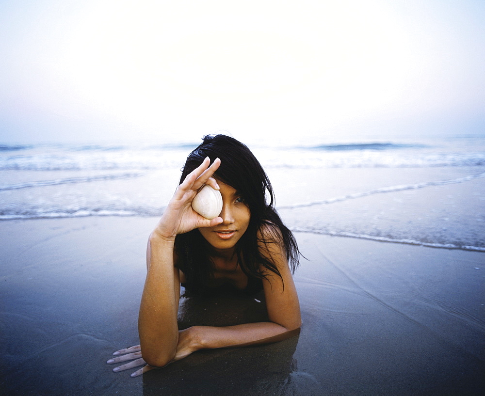 Girl lying on the beach playing with a shell