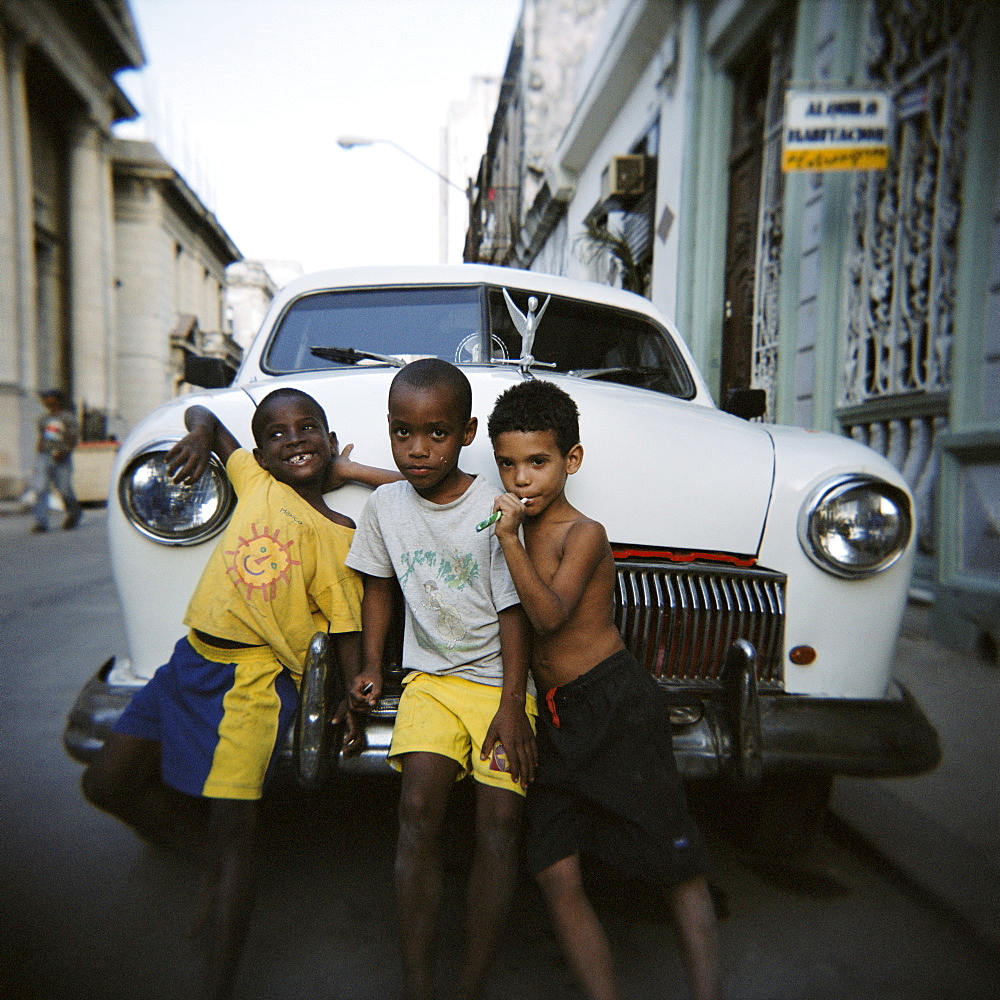 Three young boys posing against old white American car, Havana, Cuba, West Indies, Central America