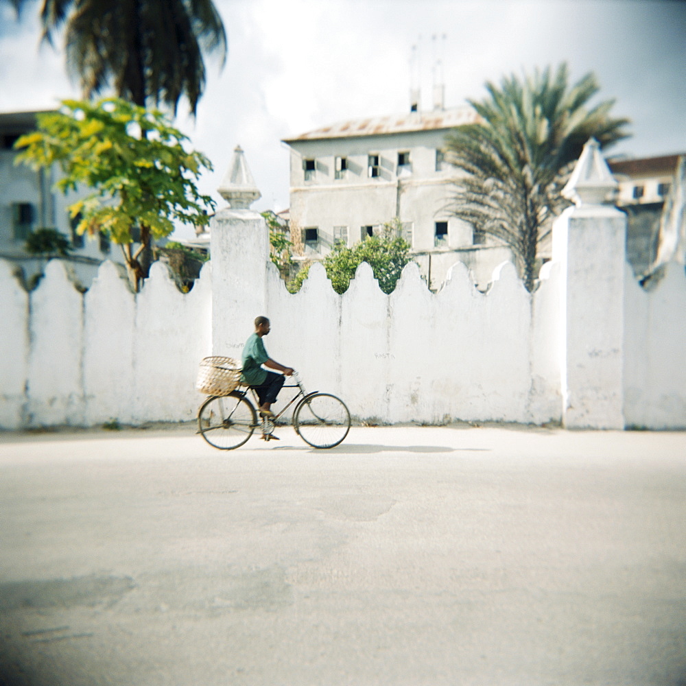 Man on bicycle with old buildings behind, Stone Town, Zanzibar, Tanzania, East Africa, Africa