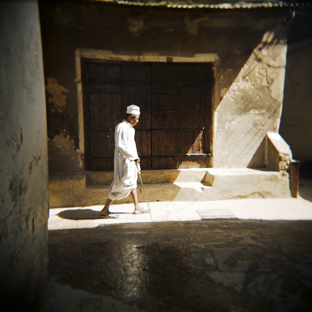 Old man walking down shady street in traditional white robes, Stone Town, Zanzibar, Tanzania, East Africa, Africa